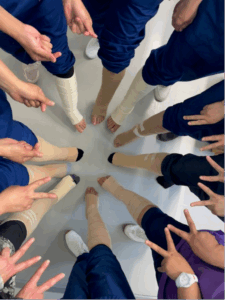 Usean henkilön kädet ja jalat ympyrässä. Kaikissa jaloissa on sideharsot