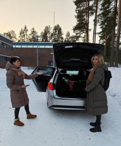 Kaksi naishenkilöä seisoo auton takana talvisessa pihassa. Auton ovet ja takaluukku ovat auki